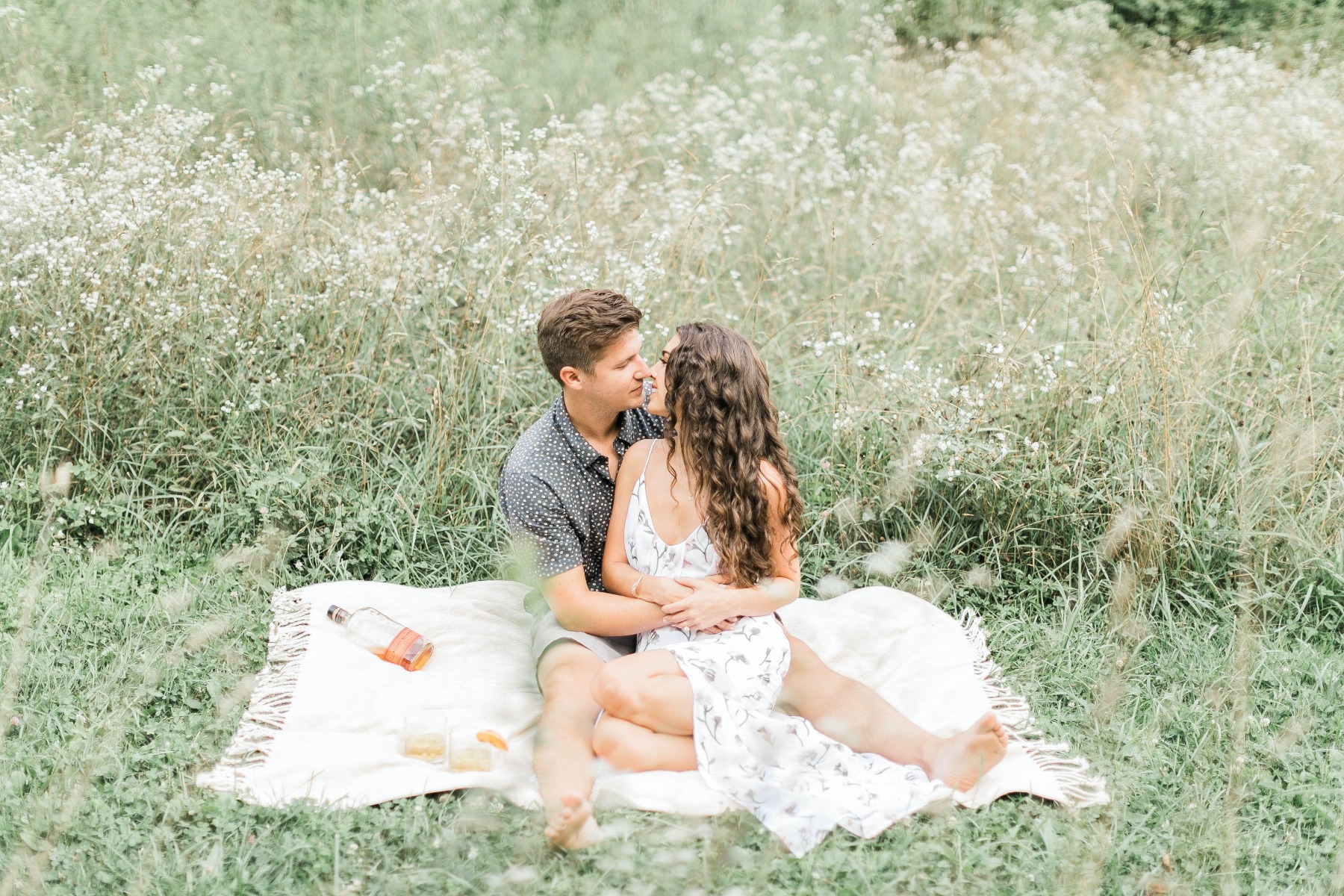 Man and woman sitting on a picnic bench showing off their engagement rings.  