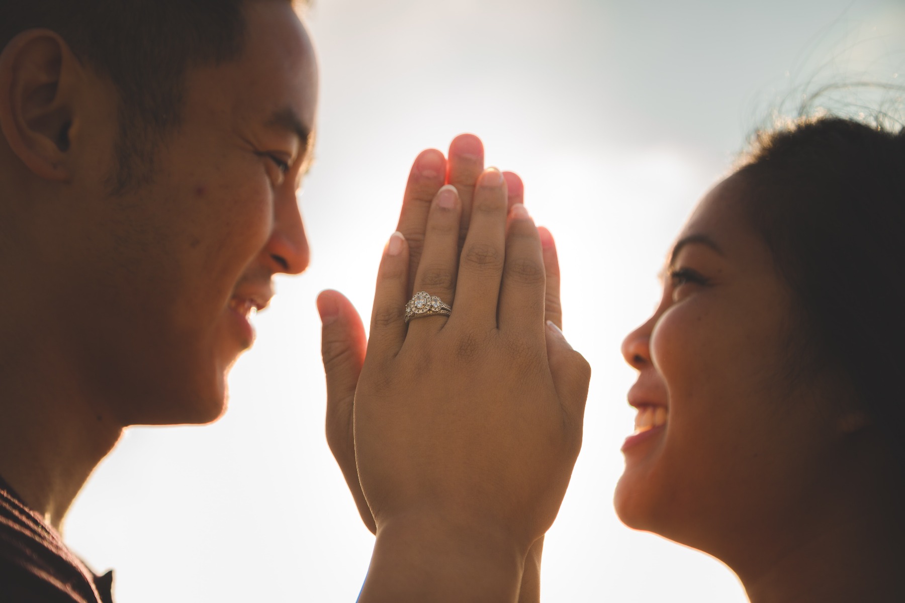 A man and a woman kissing each other while the woman holds her engagement ring up to the camera